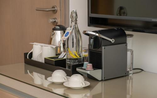 a counter top with a coffee maker and cups and a microwave at Novotel Muscat Airport in Muscat