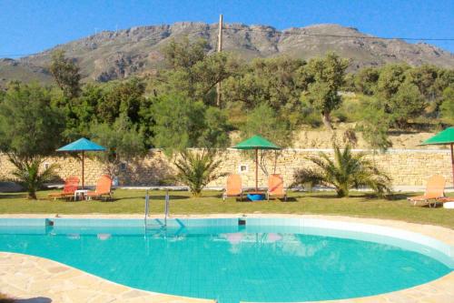 a swimming pool with chairs and umbrellas and a mountain at Petra Mare Babis in Akoumia