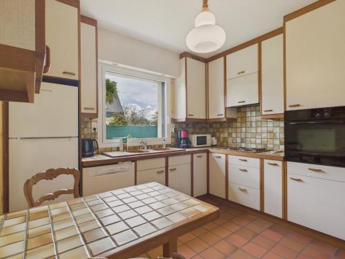 une cuisine avec des armoires blanches, une table et une fenêtre dans l'établissement Maison pour 6 avec jardin - Centre de Fouesnant, à Fouesnant