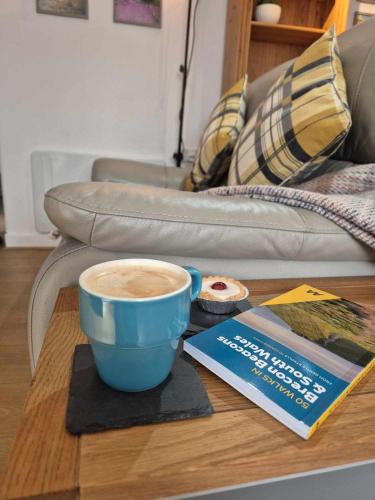 a cup of coffee on a table with a book and a couch at Sied Yr Ardd in Ystradgynlais