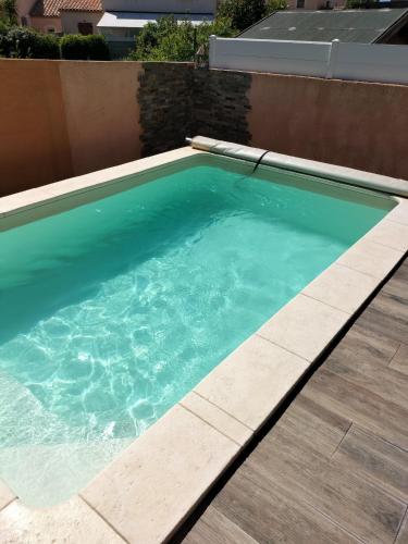 une piscine d'eau bleue et une terrasse en bois dans l'établissement Maison 100m2 plain pied 3 chambres piscine 2 places Parking, à Gigean