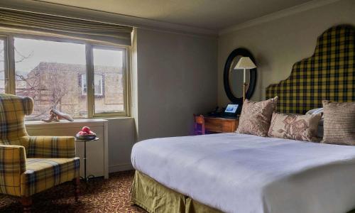 a bedroom with a bed and a chair and a window at The Lygon Arms - an Iconic Luxury Hotel in Broadway