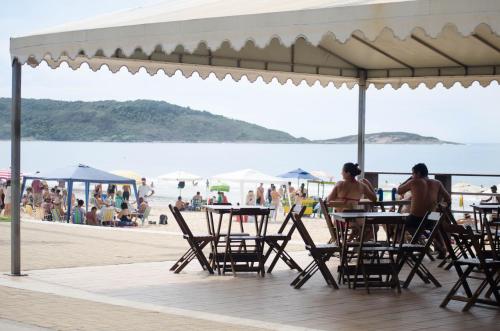 two people sitting at tables on the beach at MAIOR NOTA - 2 Quartos com AR CONDICIONADOS SPLIT, Air Fryer, Wi-Fi, Disney Plus, Star Plus, HBO Max, Guarda Sol, Cadeiras de Praia, Caixa Térmica, Churrasqueira, Rede para Descanso e Chuveirão - 8 pessoas - CONFORTO Máximo - Melhor Localização!! in Guarapari