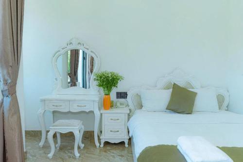 a white bedroom with a bed and a mirror at Sunrise Valley Dalat Hotel in Da Lat
