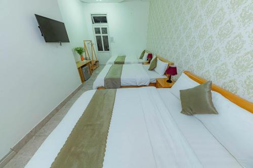 a white room with two beds and a tv at Sunrise Valley Dalat Hotel in Da Lat