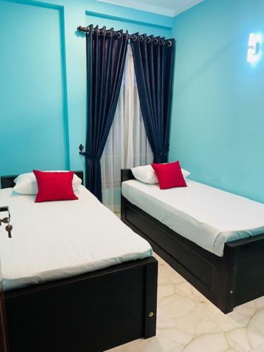 two beds with red pillows in a blue room at Kanapathiy Rest House in Trincomalee