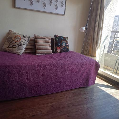 a purple bed with pillows in a room with a window at Stgo centro, Departamentos Amoblados Paz in Santiago