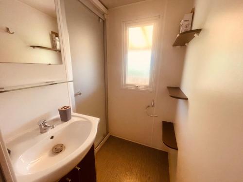 a white bathroom with a sink and a window at Mobi Home Palmiers 2 in Valras-Plage