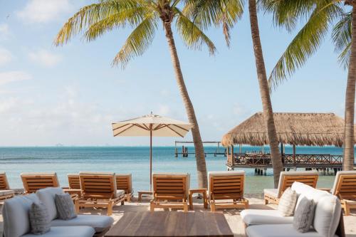 a beach with chairs and palm trees and the ocean at Almare, a Luxury Collection Resort, Isla Mujeres, Adult All-Inclusive in Isla Mujeres
