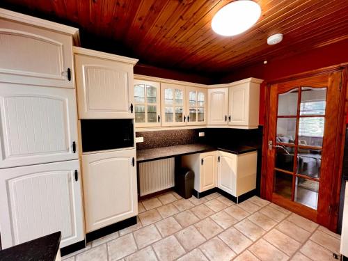 a kitchen with white cabinets and a wooden ceiling at Comfy Cottage in Ballymena