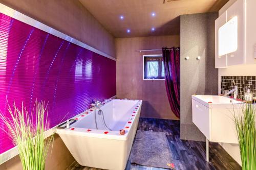 La salle de bains est pourvue d'une baignoire et d'un mur violet. dans l'établissement Maison Lili Paradis, à Saint-Savin