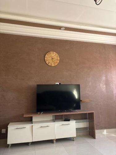 a living room with a tv and a clock on a wall at Chambre Meublée Confortable à 15 Minutes de l'Aéroport AIBD ! in Déni Diarke
