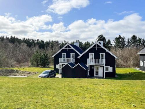 a black house with a car parked in a field at 8 person holiday home in Gjern in Gjern