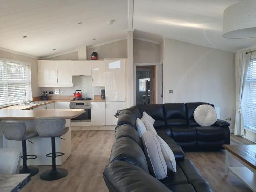 a living room with a black leather couch and a kitchen at Routh 2-Bed Luxury Lodge Hot Tub & Lake View in Routh