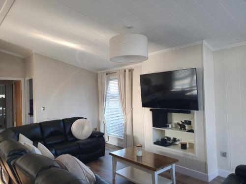 a living room with a black leather couch and a tv at Routh 2-Bed Luxury Lodge Hot Tub & Lake View in Routh