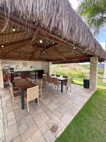 a patio with tables and chairs under a straw roof at Condomínio Alto da Serra Villas in Bananeiras