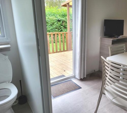 a bathroom with a toilet and a door to a deck at Mobile home 6P XL Climatisation TV WIFI parcelle XXL au calme in Ivry-la-Bataille