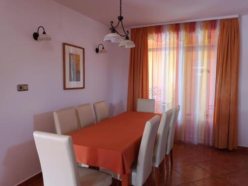 a dining room with a orange table and white chairs at Blanka Vendégház in Abádszalók
