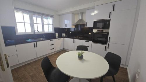 a white kitchen with a white table and chairs at Garajau Views in Caniço