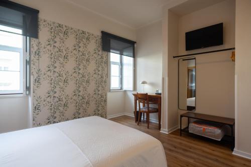 a bedroom with a white bed and a television at Hotel Vitória in Coimbra