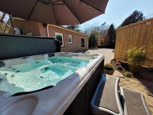 a hot tub with an umbrella in a backyard at Secret Wellness Heidezicht in Holten