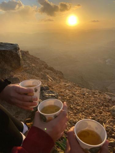 two people holding cups of coffee with the sunset in the background at נווה מדבר - צימרים ירוחם in Yeroẖam