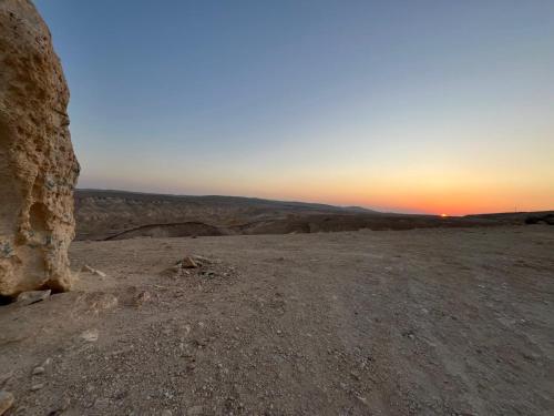 a view of the desert with the sun setting in the horizon at נווה מדבר - צימרים ירוחם in Yeroẖam