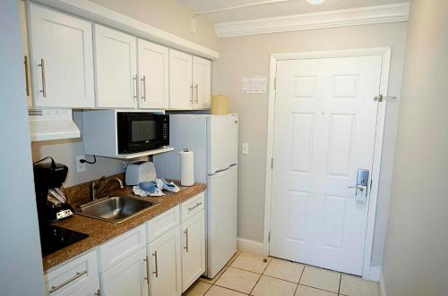 a kitchen with white cabinets and a sink and a refrigerator at The Maverick in Ormond Beach