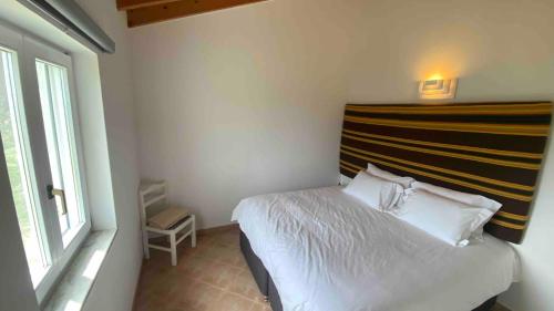 a bedroom with a white bed with a striped headboard at Vale das Estrelas in São Teotónio