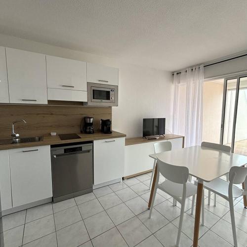 une cuisine avec des armoires blanches et une table avec des chaises dans l'établissement Appartement 4 personnes Natura Beach 106, au Cap d'Agde