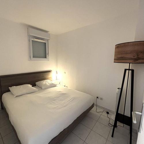 une chambre avec un lit avec des draps blancs et une lampe dans l'établissement Appartement 4 personnes Natura Beach 106, au Cap d'Agde
