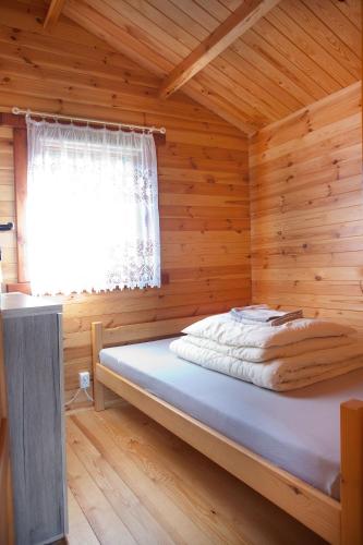 a bed in a wooden room with a window at Domki letniskowe KEYA in Gąski