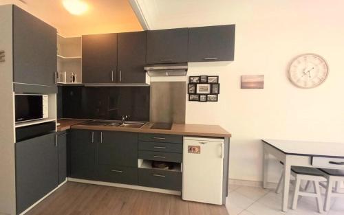 une cuisine avec des armoires noires, une table et une horloge dans l'établissement Résidence Houle - Studio neuf pour 2, à deux pas des plages d'Arcachon MAE-8324, à Arcachon
