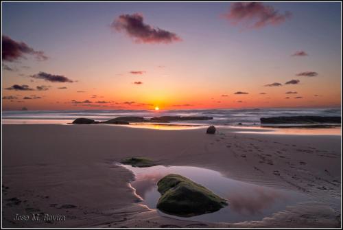 a sunset on a beach with rocks in the sand at Chateau La Roca in Sancibrián