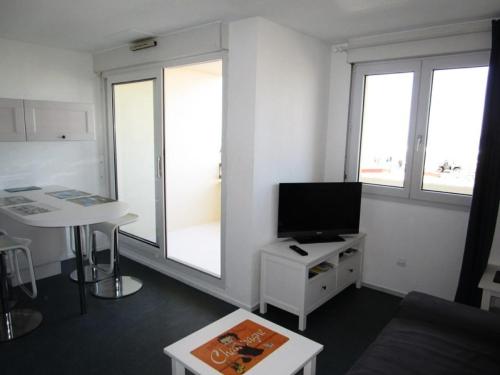 Il comprend un salon doté d'une télévision, d'une table et de fenêtres. dans l'établissement Résidence Ortal - Charmant appartement 4 personnes front de mer à Lacanau Océan MAE-0341, à Lacanau
