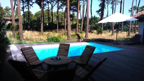 - une piscine avec 2 chaises, une table et un parasol dans l'établissement Résidence 05023m-lacanau Ocean - Grande villa 5 chambres pour 12 personnes avec piscine privée, plage à pieds, Lacanau Océan MAE-0421, à Lacanau