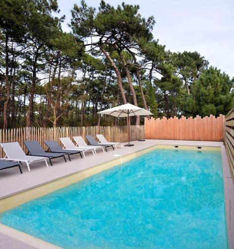 - une piscine avec des chaises et un parasol à côté d'une clôture dans l'établissement Résidence Margalex - Maison mitoyenne dans belle résidence neuve, piscine collective à Lacanau Océan MAE-0681, à Lacanau