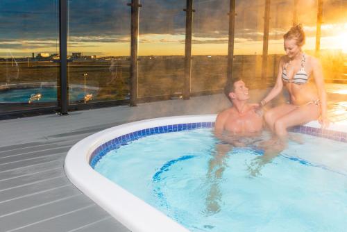 a man and a woman sitting in a swimming pool at Applause Hotel Calgary Airport by CLIQUE in Calgary