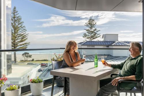 a man and a woman sitting at a table on a balcony at Spectacular Sunrises & Sea Views - Pool Spa Gym in Mount Maunganui