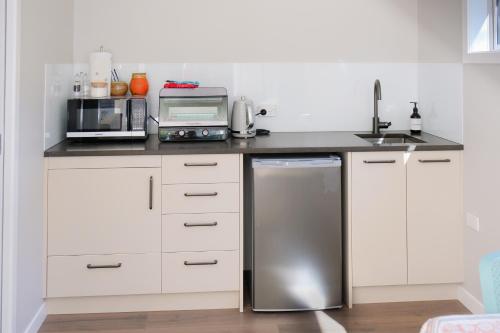 a kitchen with white cabinets and a stainless steel refrigerator at Studio Wing in Saint Heliers in Auckland