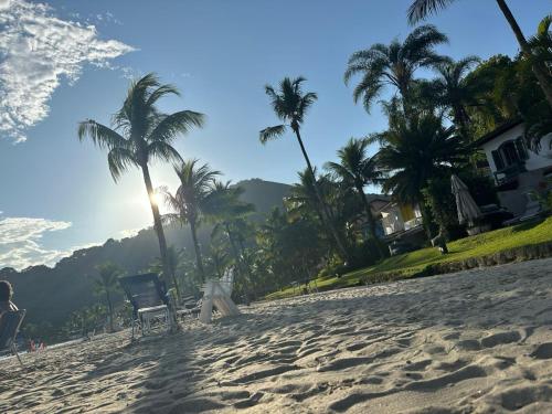 a beach with palm trees and a chair on it at Suíte 3 Vila dos Pescadores Condomínio Portogalo in Angra dos Reis