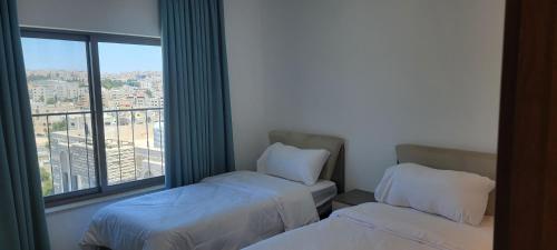 two beds in a room with a large window at مراسيم للشقق الفندقية in Amman