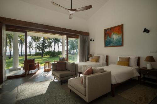 a bedroom with a bed and a couch and chairs at Kalkudah Beach House in Batticaloa