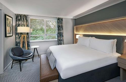 a hotel room with a large bed and a chair at Hilton Cobham in Cobham
