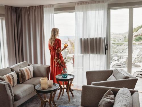 a woman standing in a living room looking out the window at Smögens Hafvsbad in Smögen