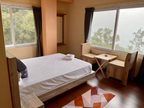 a bedroom with a bed and a chair and windows at Lamahatta Clouds Hotel & Restaurant in Takdāh