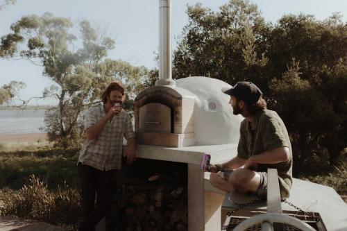 two people are standing next to an outdoor oven at Waterfront - Hot Tub - Sauna - Serenity in Coles Bay
