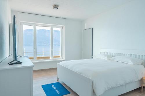 ein weißes Schlafzimmer mit einem Bett und einem Fenster in der Unterkunft Duplex Lakeside Penthouse in Porto Valtravaglia