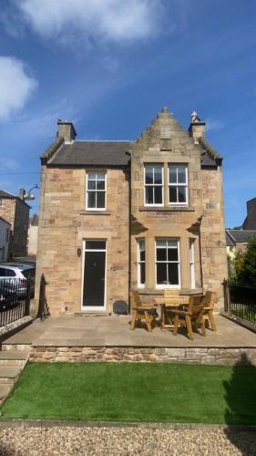 a stone house with picnic tables in front of it at Abbey House Charming traditional historic house in Jedburgh
