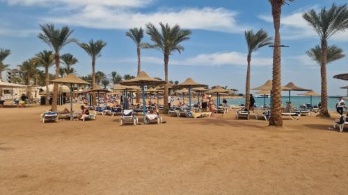 a beach with chairs and umbrellas and palm trees at Hurghada Mirage Bay Resort & Aquapark in Hurghada
